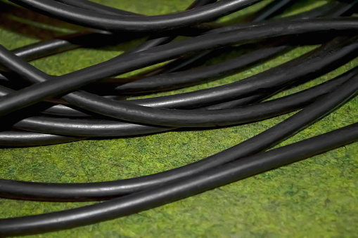 Black wire on the green carpet. There is a reeled black cable on the floor. A thick wire of black color in a winding on a green carpet.