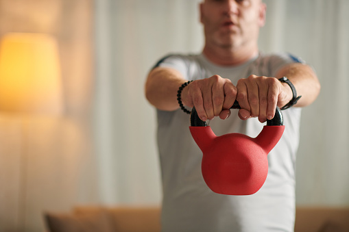 Cropped image of mature sportsman lifting kettlebell, arms exercise concept