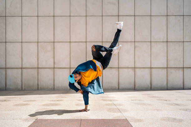 Hip Hop Dancer in the Street Talented young man doing break dance dances against white wall in the street and looking at camera. breakdance stock pictures, royalty-free photos & images