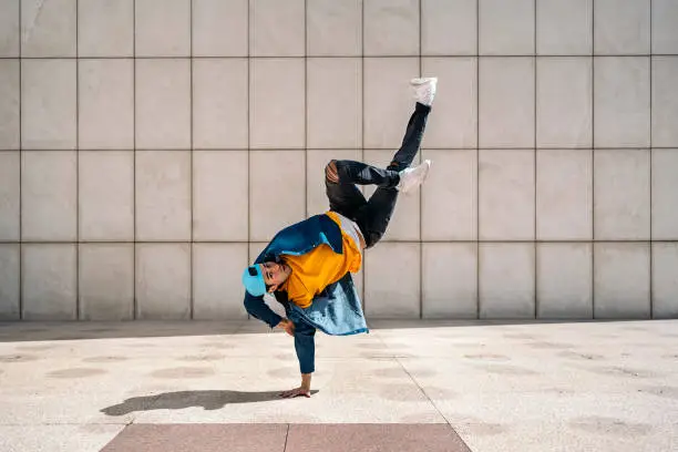 Talented young man doing break dance dances against white wall in the street and looking at camera.