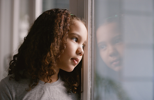 Child waiting, thinking and looking out a home window alone in a house bored by the windows, Kid, girl and young person look outdoor feeling calm, relax and lonely or sad with contemplation