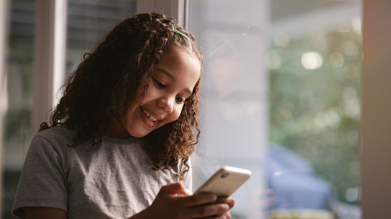 Phone, social media and children with a girl typing a text message or browsing the internet in her home. Kids, smartphone and communication with a female child texting or reading online in a house