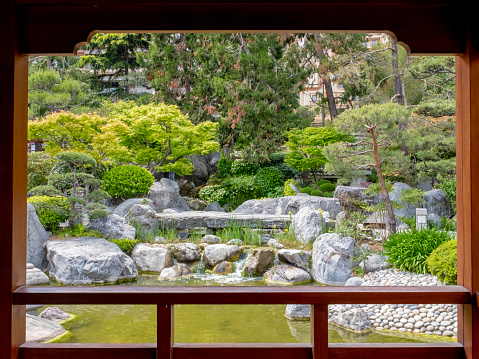 Monaco - May 3, 2022: A pond and a waterfall seen from a wood pavilion of the Japanese garden of Monaco. Taken on a sunny spring day.