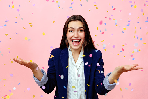Studio portrait of young woman smiling with confetti falling against pink background