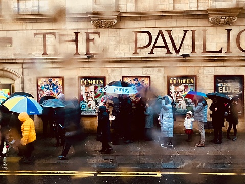 People queuing for the The Pavilion theatre in the rain with umbrellas on Boxing Day 2022 in Glasgow City centre