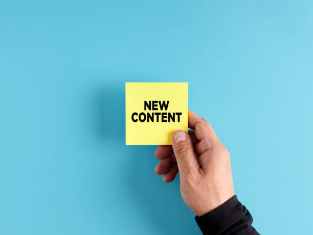 istock Male hand holds a yellow sticky note paper with the message new content. New content announcement. 1452665565