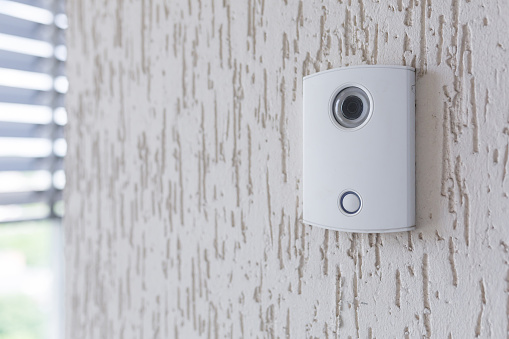 A white incoming electronic doorbell with a camera on the wall of the building, office