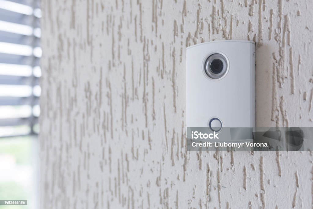 A white incoming electronic doorbell with a camera on the wall of the building, office A white incoming electronic doorbell with a camera on the wall of the building, office. Ring - Jewelry Stock Photo