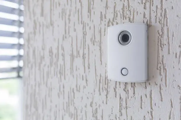 A white incoming electronic doorbell with a camera on the wall of the building, office.
