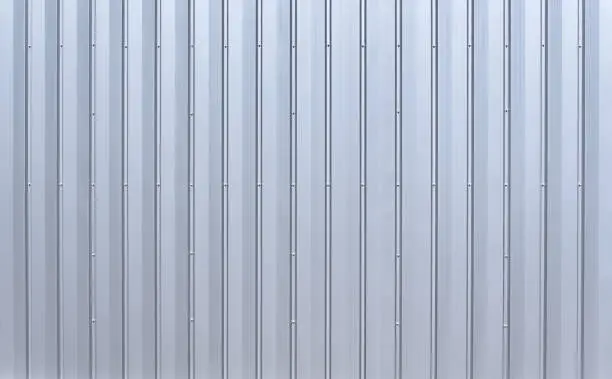 Silver colored aluminum wall paneling with vertical grooves and several rows of hex bolts