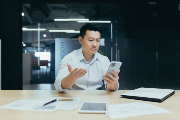 istock Confused Asian guy holding smart phone feels concerned thinking over received message. Mobile phone everyday usage, unpleasant news, waiting for important call, low signal device problems concept. 1452667975