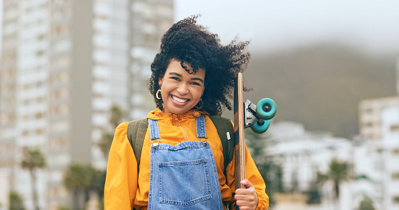 Young black woman, skateboard and urban in city portrait, smile and trendy skateboarder, happy in Los Angeles. Young, African American gen z youth in wind and skateboarding, happy in cityscape.