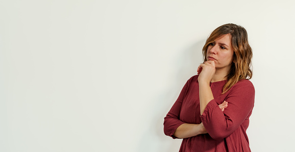 worried and pensive woman with her hand on her chin on a white background looking at the copy space