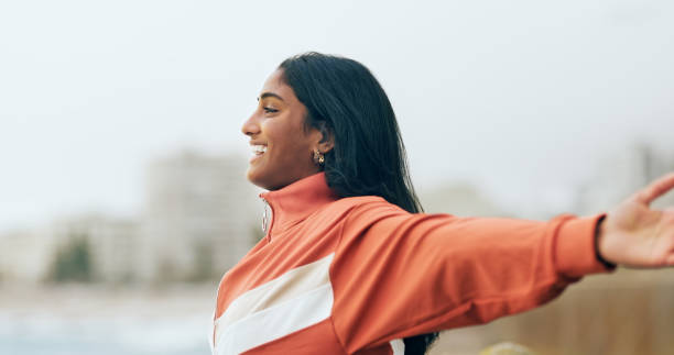 mujer india feliz, libertad al aire libre y brazos extendidos, viento del océano y respirar aire fresco con propósito o felicidad, motivación y bienestar, paz y esperanza. sonrisa, optimismo y sueño, éxito en la naturaleza - bienestar mental fotografías e imágenes de stock