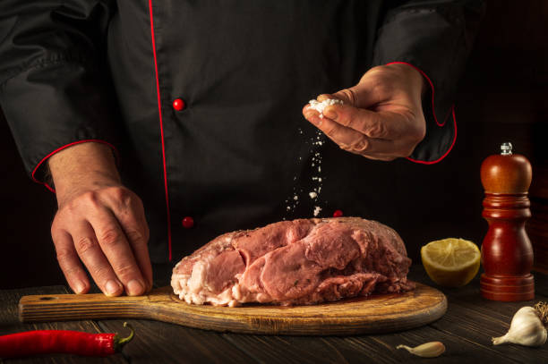 istock Professional chef sprinkles raw meat with salt. Preparing fresh meat before roasting. Menu concept for restaurant or hotel. European cuisine 1452670779
