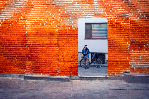A cyclist takes a picture of himself through a wall mirror on an orange brick street