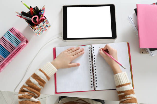 istock Cute little girl with modern tablet studying online at table, top view. E-learning 1452670994