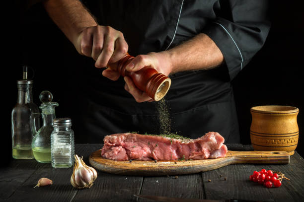 un chef professionnel prépare de la viande de veau crue. avant la cuisson, le chef ajoute du poivre au bœuf. un plat national est en cours de préparation dans la cuisine du restaurant - veal calf meat baking photos et images de collection