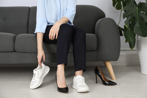 Woman changing shoes on sofa in office, closeup