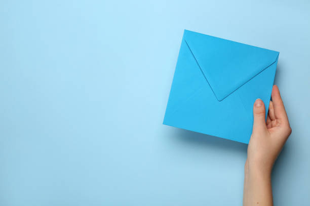 istock Woman holding envelope on light blue background, top view. Space for text 1452677529