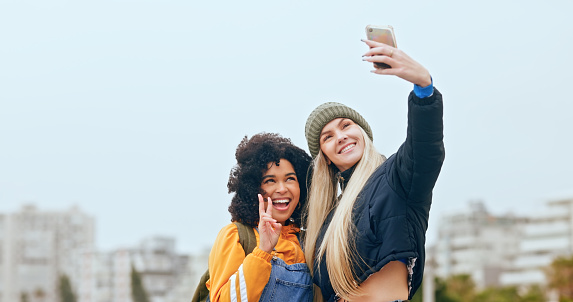 Friends, selfie and trendy or stylish women bonding in the city and having fun while taking a photo. Hand gesture, mobile picture and social media of girls bond with happiness in an urban town