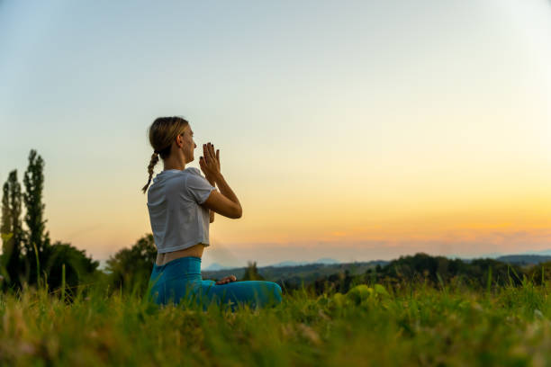 istock Woman meditating in prayer pose on grassy landscape 1452680092