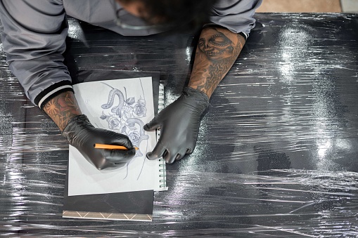 A tattoo artist is drawing a design stencil on his work stretcher before tattooing. Concept of artist inspiration