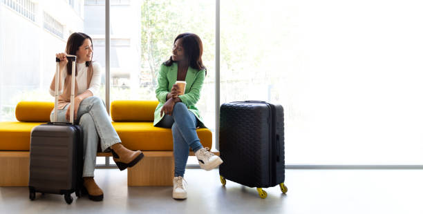 Horizontal banner image of multiracial women sitting on hotel reception bench talking. Copy space.