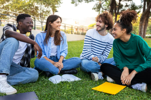 istock Multiracial college students study together sitting on campus grass. Friends talking in park. 1452682445