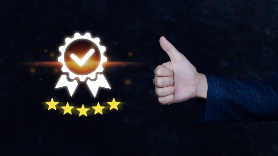 Businessman hand shows the symbol of the top service Quality assurance 5 star with thumb up , Guarantee, best product, Standards, ISO certification and standardization concept.