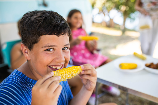 A cute boy is munching on a corn on the cob while on a family camping trip