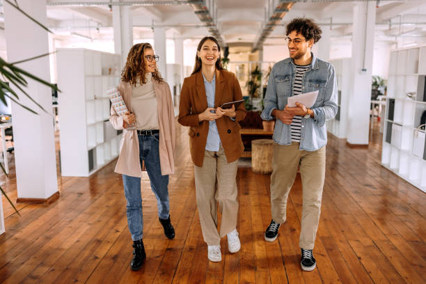 Group of smiling young colleagues walking and talking in modern office stock photo