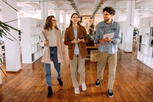 Photo of Group of smiling young colleagues walking and talking in modern office