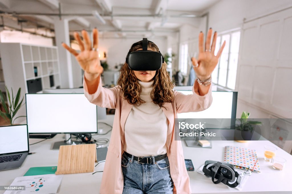Young beautiful woman using VR goggles in the modern office Virtual Reality Simulator Stock Photo