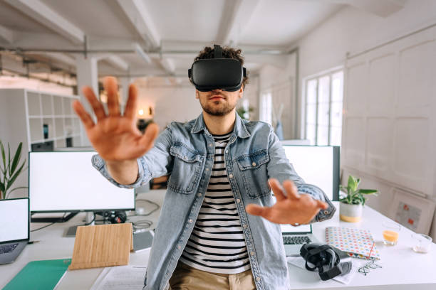 Young handsome casually clothed man using VR goggles in the modern office