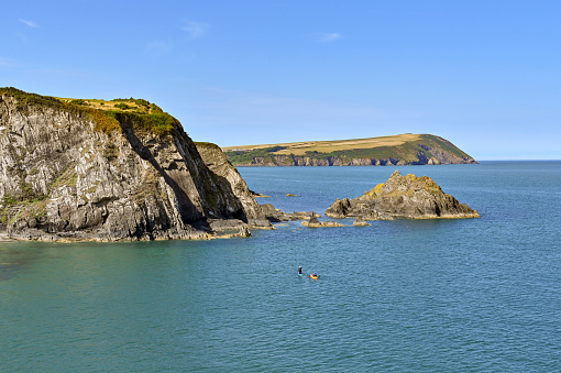 Newport, Pembrokeshire, Wales - August 2022: Person on a paddleboard and a person in a kayak near the headland of the bay
