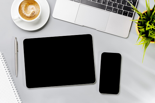 Tablet and smartphone with blank screen on business office desk. Flat lay workspace with sunny light and copy space