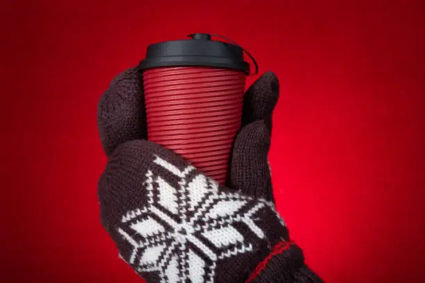 hands with gloves and holding cup of hotdrink on a red background horizontal composition