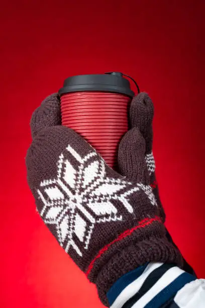 hands with gloves and holding cup of hotdrink on a red background vertical composition