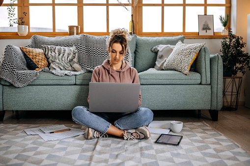 Young beautiful woman studying while sitting on the floor at her small cozy apartment