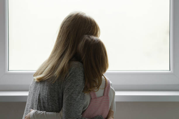 giovane madre adulta e figlia insieme guardando fuori dalla finestra di casa. concetto di attesa, desiderio o tristezza. primo piano. vista posteriore. - pensive only baby girls baby girls baby foto e immagini stock