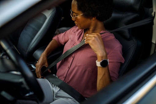 Portrait of responsible mid adult African American woman sitting in the driver's seat of her car and fastening a seat belt before driving to work.