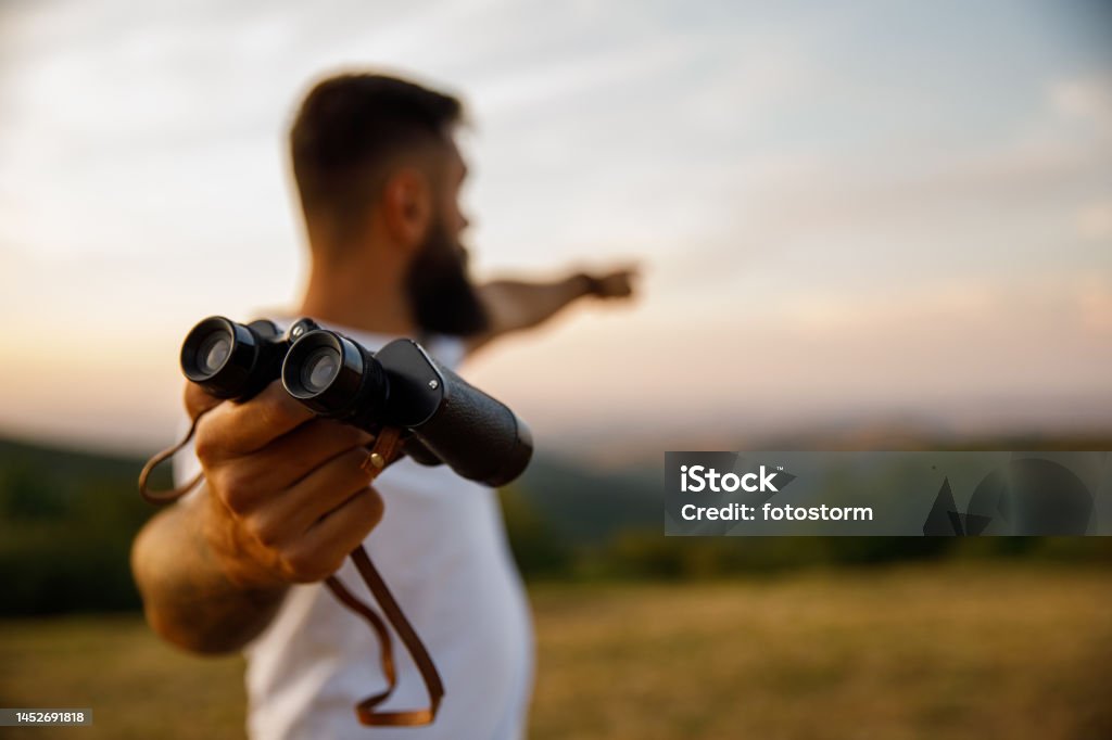 Man giving you binoculars and pointing in the distance to where to look Copy space shot of young male hipster giving you binoculars and pointing in the distance, to where to look at while standing on the viewpoint. Binoculars Stock Photo