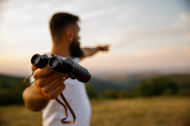 Man giving you binoculars and pointing in the distance to where to look stock photo