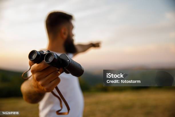 Man Giving You Binoculars And Pointing In The Distance To Where To Look Stock Photo - Download Image Now
