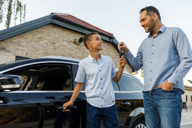Father giving car keys to his teenage son when teaching him how to drive Candid shot of caring mid adult man handing car keys to his teenage son while they are standing by the car, about to teach him how to drive for the first time. teenager boy driving stock pictures, royalty-free photos & images