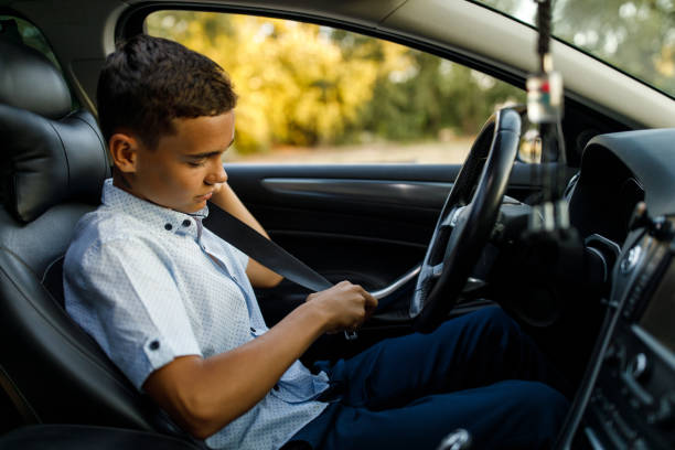 Teenage boy sitting in driver's seat and fastening a seat belt Profile view of responsible teenage boy sitting in driver's seat and fastening a seat belt. teenager boy driving stock pictures, royalty-free photos & images