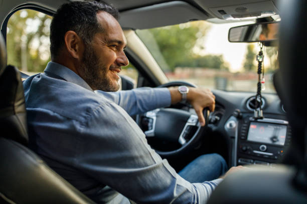 Joyful mid adult man smiling at his teenage son sitting in the passenger’s seat stock photo