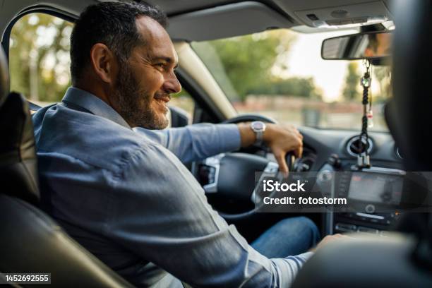 Joyful Mid Adult Man Smiling At His Teenage Son Sitting In The Passengers Seat Stock Photo - Download Image Now