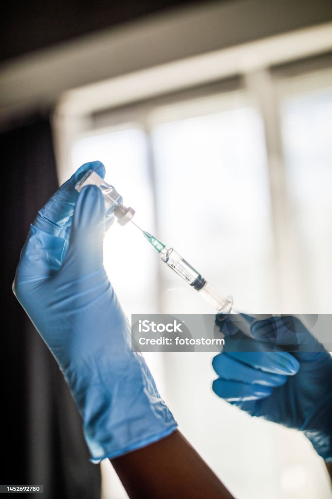 Nurse wearing disposable gloves and preparing a vaccine or a shot in a syringe Close up shot of unrecognizable nurse, wearing disposable gloves, preparing a vaccine or a shot in a syringe. She is drawing medicine from a vial. 20-24 Years Stock Photo